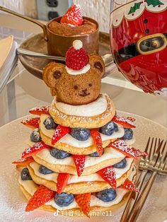 a teddy bear sitting on top of a stack of pancakes with strawberries and blueberries