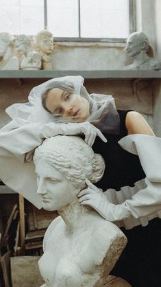 a woman standing next to a white busturine in a room filled with statues