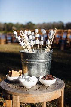 marshmallows and chocolate on sticks in a metal bucket with spoons next to it