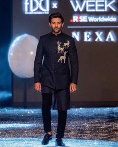 a man is walking down the runway wearing a black outfit with reindeer designs on it