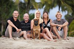 a group of people sitting on top of a sandy beach next to a brown dog