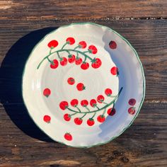 a white plate with red cherries on it sitting on a wooden table next to a knife and fork