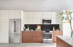 a modern kitchen with stainless steel appliances and wood cabinetry, along with white walls