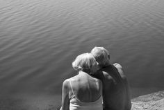 two people sitting on the edge of a body of water looking at something in the distance