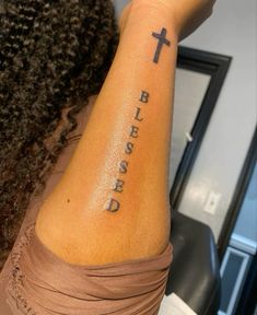 a woman with a cross tattoo on her arm and the words, be blessed written in cursive font