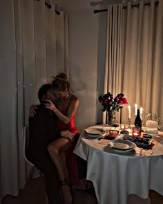 two people sitting at a table with food and wine in front of them, one woman is hugging the other