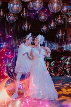 two women in white dresses are dancing with disco balls