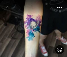 an arm with a saturn tattoo on it and watercolor paint splatters all over it