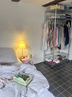 a room with a bed, lamp and clothes on racks in it's corner