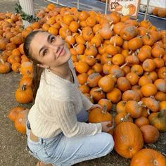 a woman sitting on the ground surrounded by pumpkins