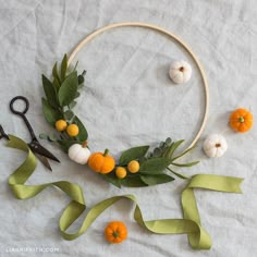 an orange and white wreath with green leaves on it next to scissors, ribbon and pumpkins