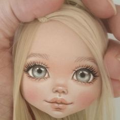 a close up of a doll with long blonde hair and blue eyes holding it's head