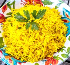 yellow rice is on a colorful plate with flowers and green leafy leaves around it