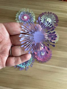 a hand holding some paper flowers on top of a wooden table