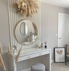 a white dressing table with a round mirror on the wall and a stool in front of it