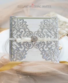 a white and silver wedding card on top of a plate with gold ribbon around it