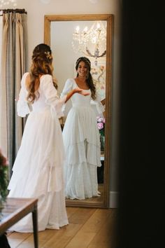 a woman in a white dress is looking at herself in the mirror while another person stands nearby