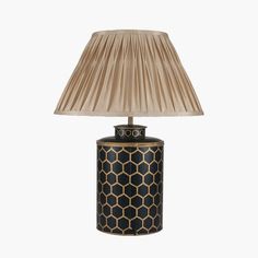 a black and gold table lamp with a beige shade on the top, sitting against a white background