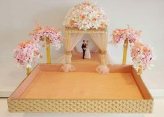 a wedding cake with pink flowers on top and a man and woman in the background