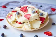 a plate filled with sliced up fruit on top of a white table next to blueberries and strawberries