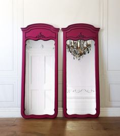 two pink mirrors sitting on top of a wooden floor next to a wall mounted chandelier