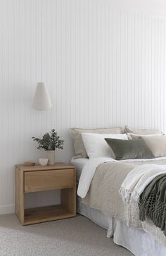 a bed with white sheets and pillows next to a night stand on carpeted floor