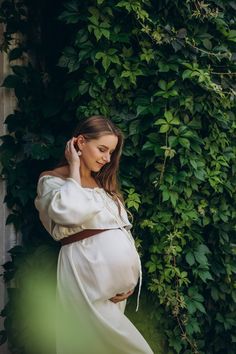 a pregnant woman in a white dress is talking on her cell phone while leaning against a green wall