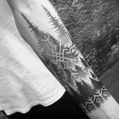 black and white photo of a person with a tattoo on his arm, standing next to a wall