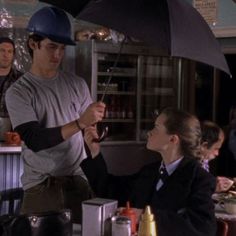 a man holding an umbrella while standing next to a woman sitting at a table in front of him