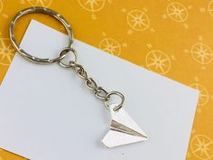 a metal keychain with a paper airplane on it's side sitting on top of a piece of white paper