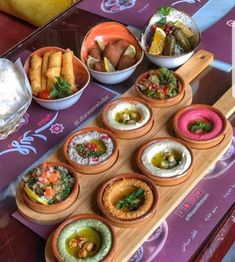 a table topped with bowls filled with different types of food and dipping sauces on top of wooden trays