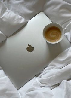 an apple laptop on a bed with a cup of coffee in front of the screen