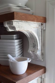 a stack of white dishes sitting on top of a wooden shelf next to a bowl