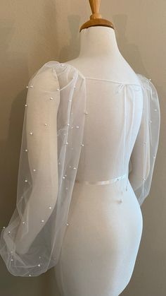 a mannequin wearing a white dress with sheer sleeves and pearls on it's back