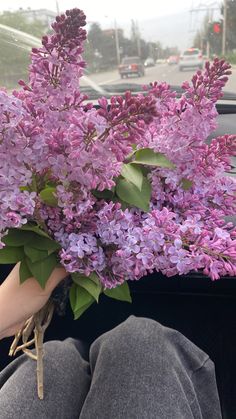 a person is sitting in the back seat of a car holding a bouquet of lilacs