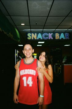 a young man and woman standing in front of a snack bar with their arms around each other