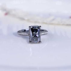 an engagement ring with a cushion cut gray diamond surrounded by pave diamonds on a white surface