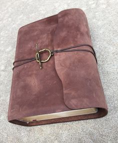 a brown leather journal with a gold clasp on the front cover is laying on concrete