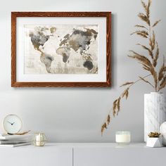 a white dresser topped with a vase filled with plants and a framed world map on the wall