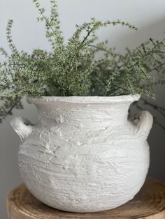 a white vase sitting on top of a wooden table next to a planter filled with greenery