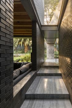 a long hallway with brick walls and steps leading up to the second floor, surrounded by greenery