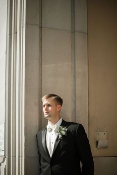 a man in a tuxedo standing next to a tall column with his hands in his pockets