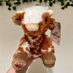 a hand holding a brown and white giraffe stuffed animal with tags on it's ears