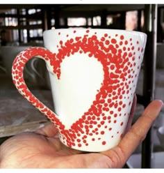 a hand holding a coffee cup decorated with red and white dots in the shape of a heart