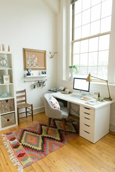 a desk with a computer on top of it next to a chair and bookshelf