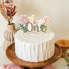 a white cake sitting on top of a wooden plate next to a vase with flowers