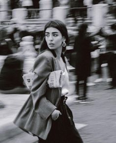 a woman walking down the street while wearing a coat and holding a cup in her hand