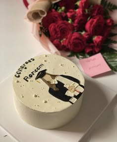 a white cake sitting on top of a table next to red roses and a bouquet