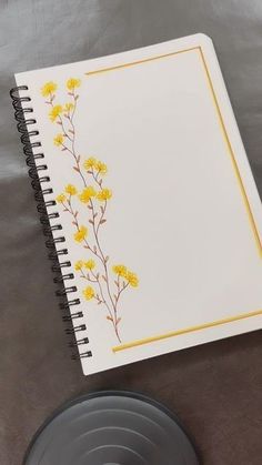 a spiral notebook with yellow flowers on it sitting next to a black plate and saucer