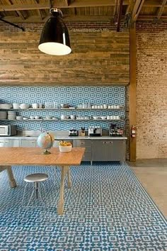 an open kitchen with blue tiles on the floor and wooden walls, along with a dining table